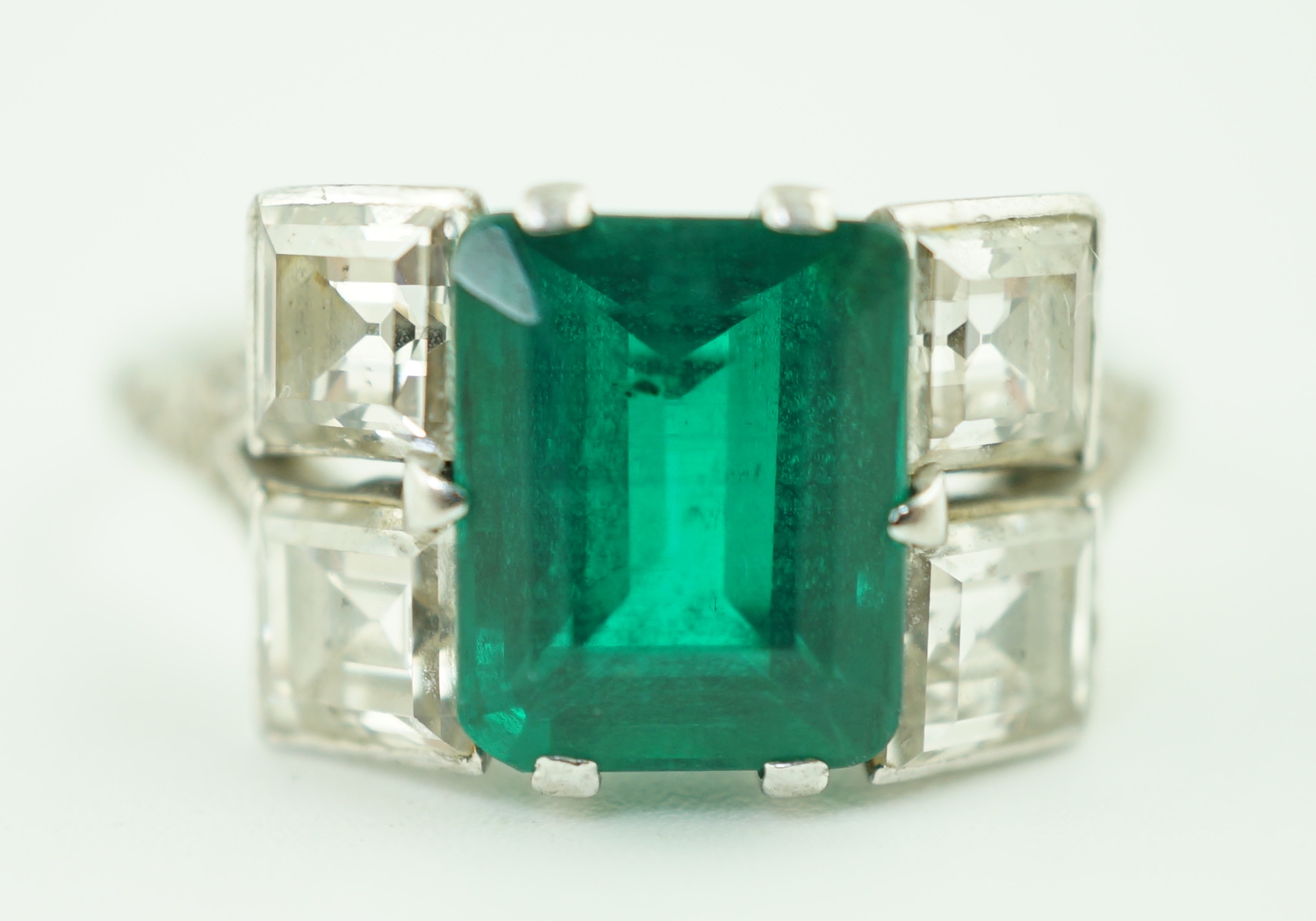 An Art Deco platinum, emerald and square cut diamond dress ring, with diamond chip set shoulders